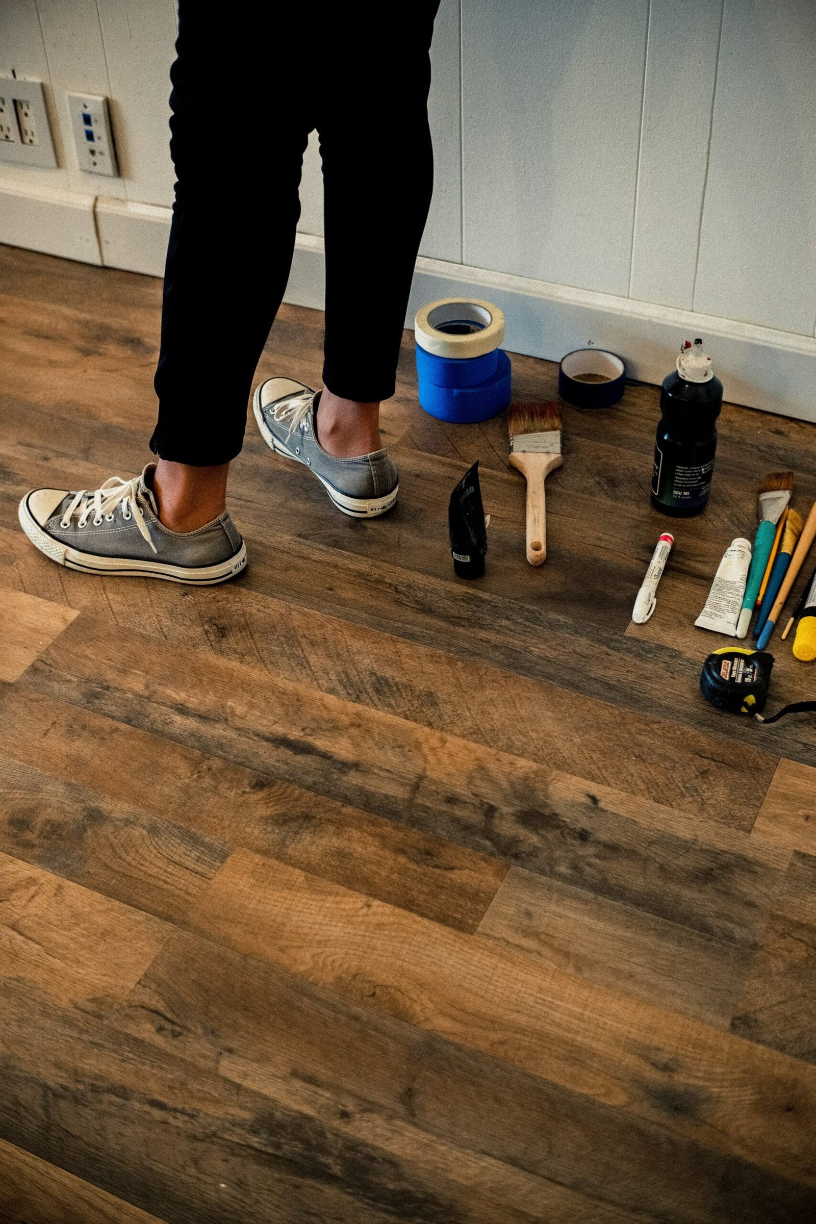 person in black pants and white and black nike sneakers standing on brown wooden floor